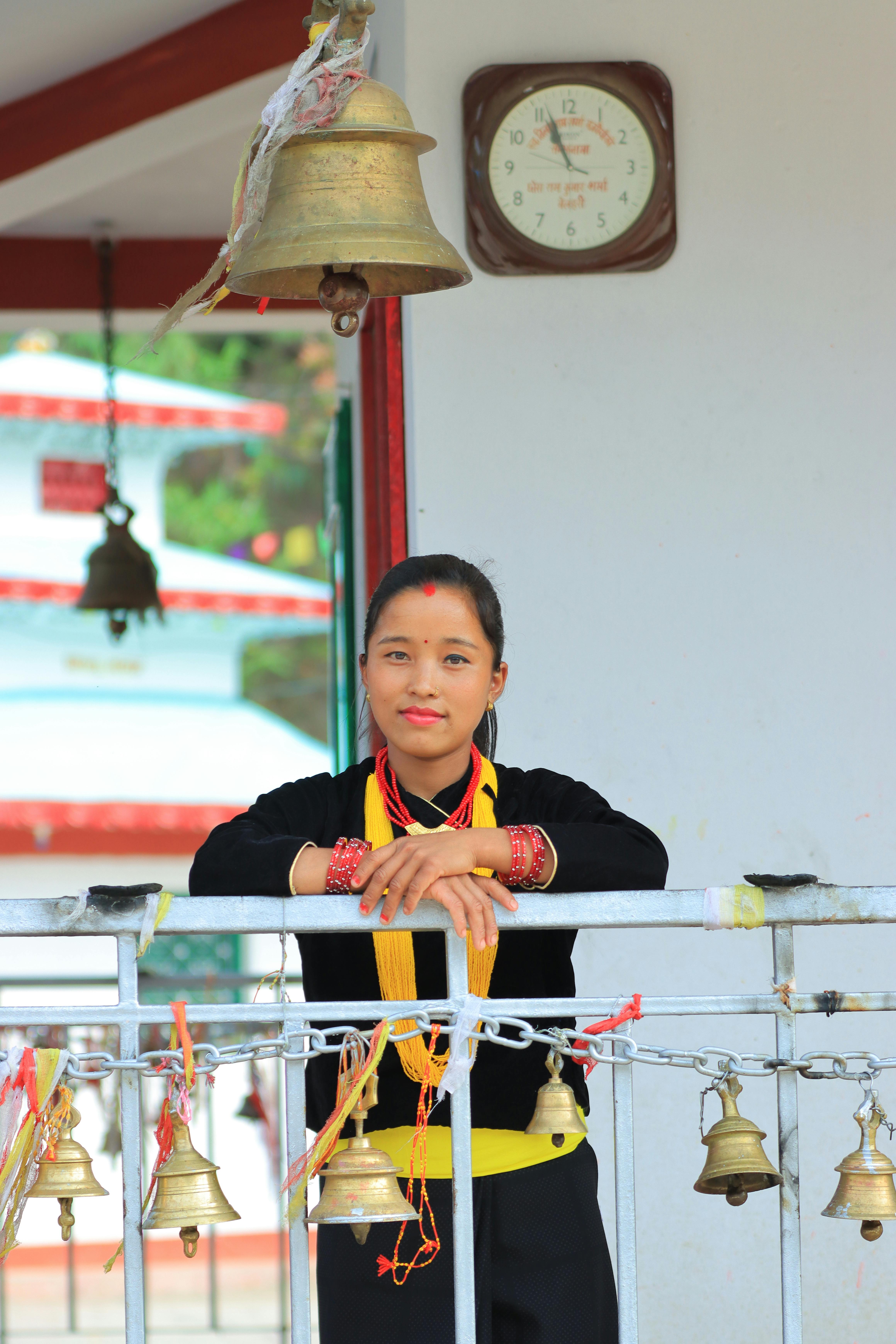 A woman in traditional attire poses by temple bells, showcasing cultural heritage.