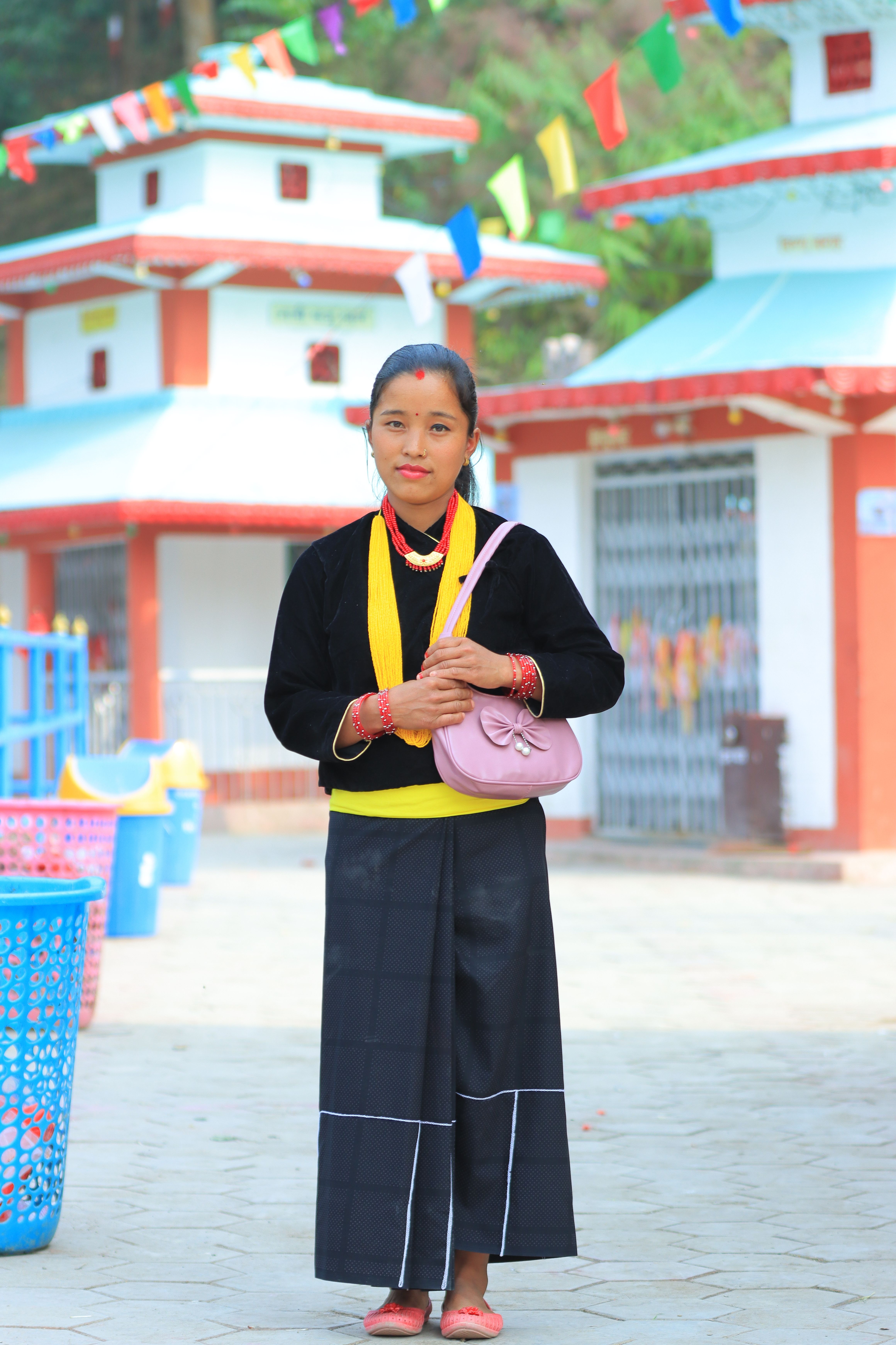 Woman in traditional attire standing in front of a temple with colorful flags.