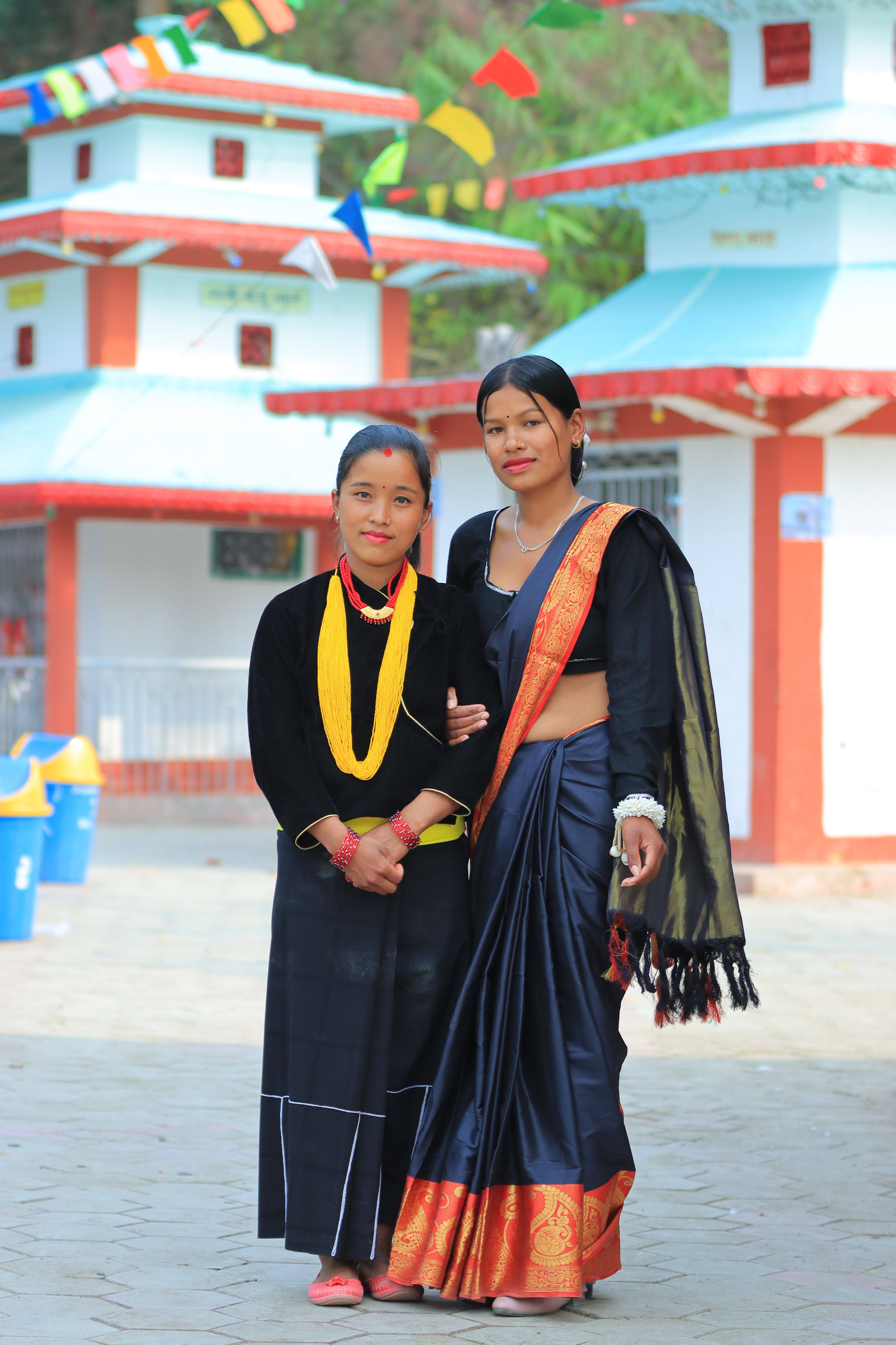 Two women in traditional attire standing outside a colorful temple.