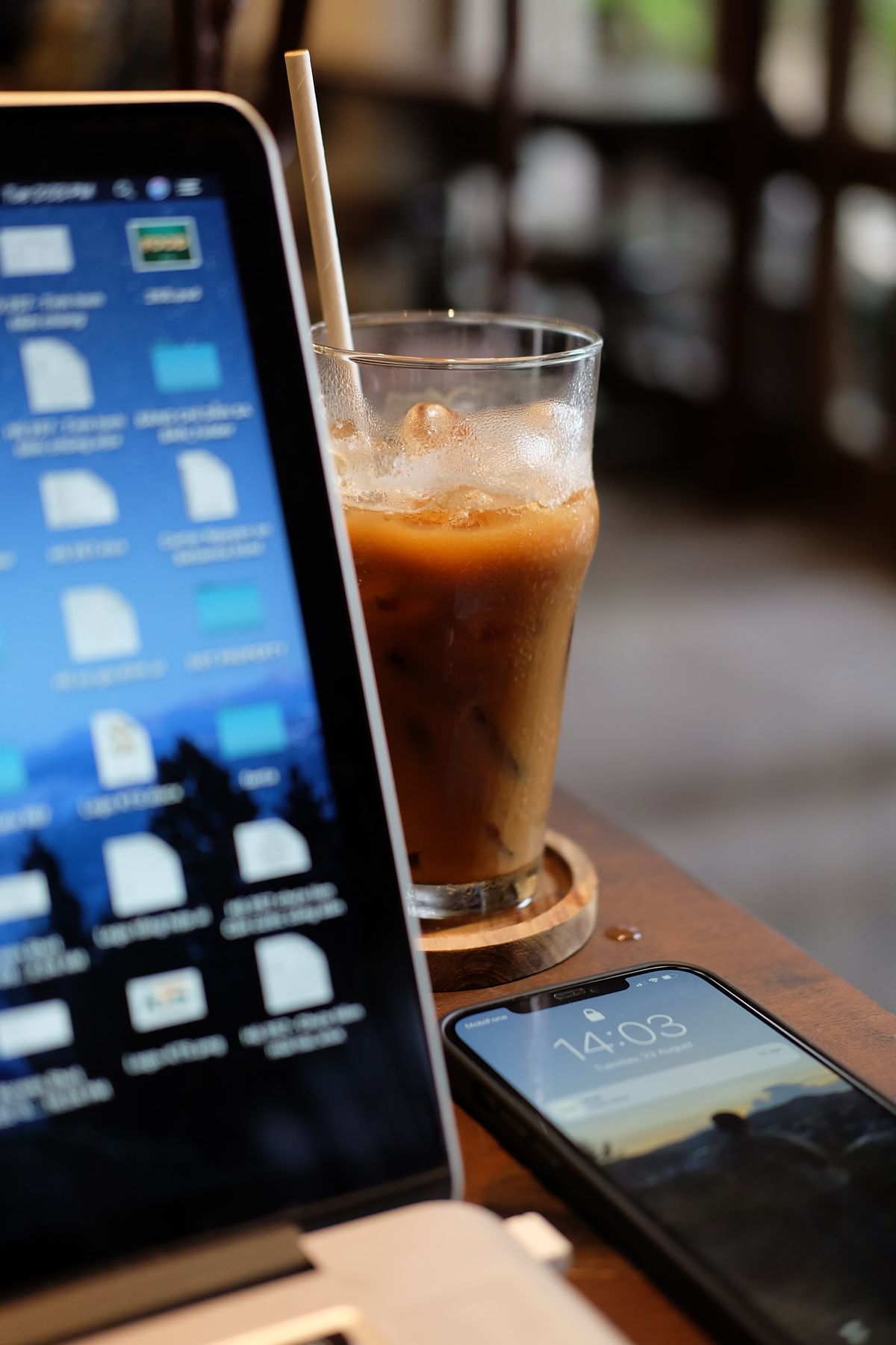 A cozy coffee shop workspace setup with a laptop, iced coffee, and smartphone