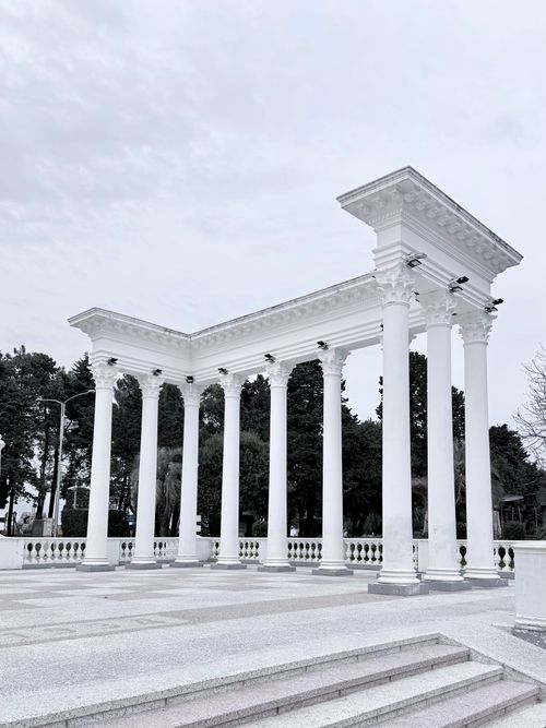 Free Elegant white colonnade against lush greenery in urban park, conveying architectural beauty. Stock Photo