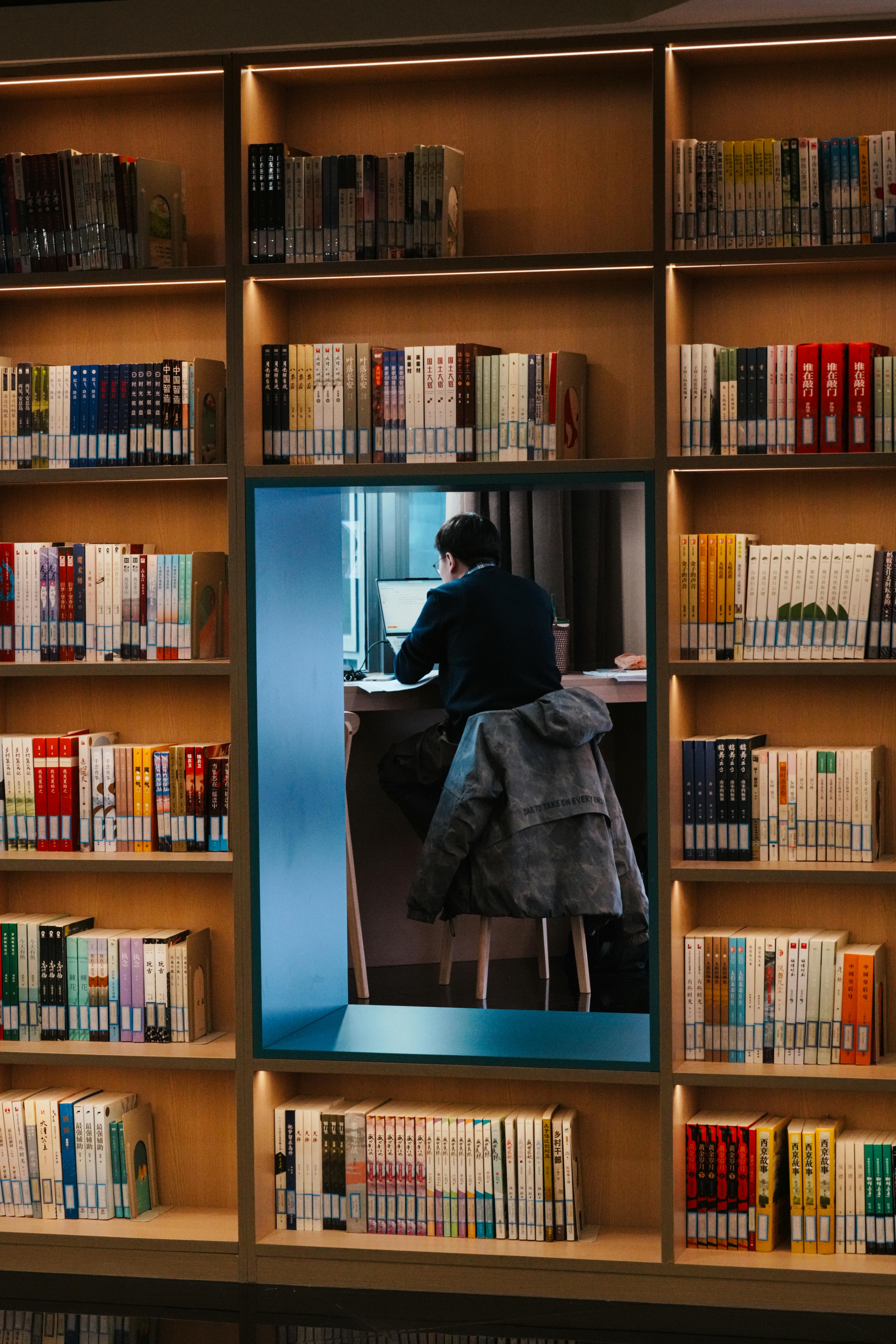 Man Reading in Library Surrounded by Bookshelves