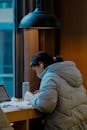 Young Woman Studying by a Window in Cozy Jacket