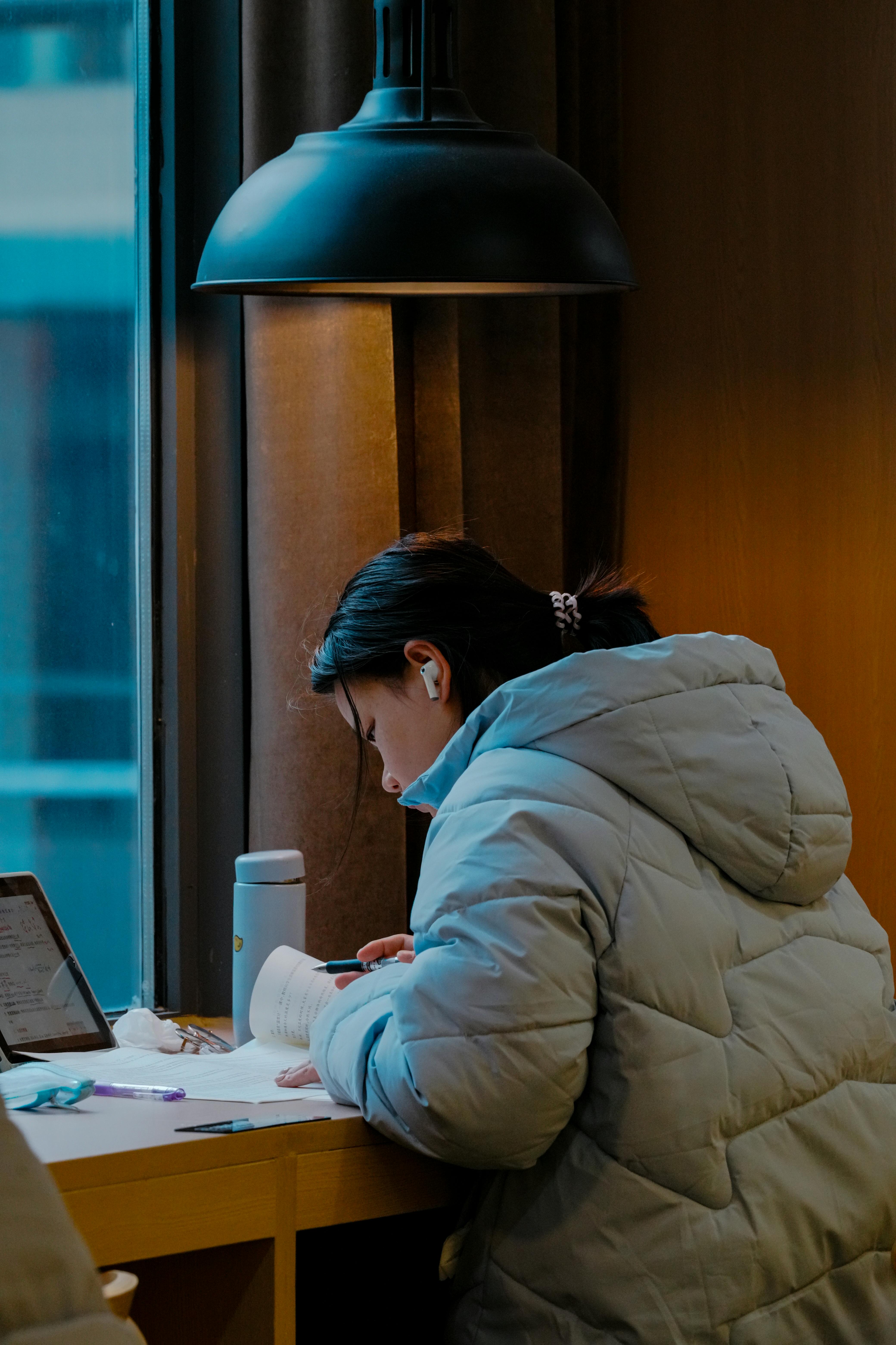 Young Woman Studying by a Window in Cozy Jacket