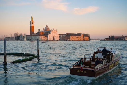 A scenic view of San Giorgio Maggiore in Venice at sunset, with a passenger boat in the foreground.