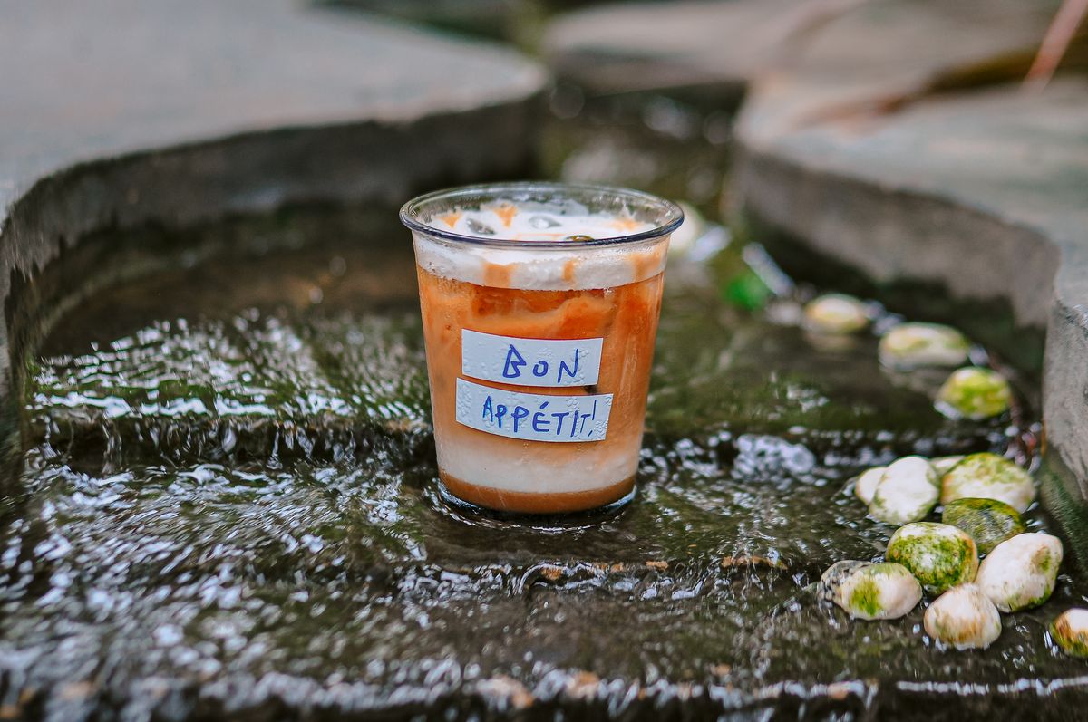A refreshing iced coffee cup with 'Bon Appétit' label, placed in a serene stream setting.