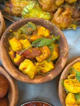 Close-up of vibrant paneer curry served in traditional clay bowl, garnished with herbs.