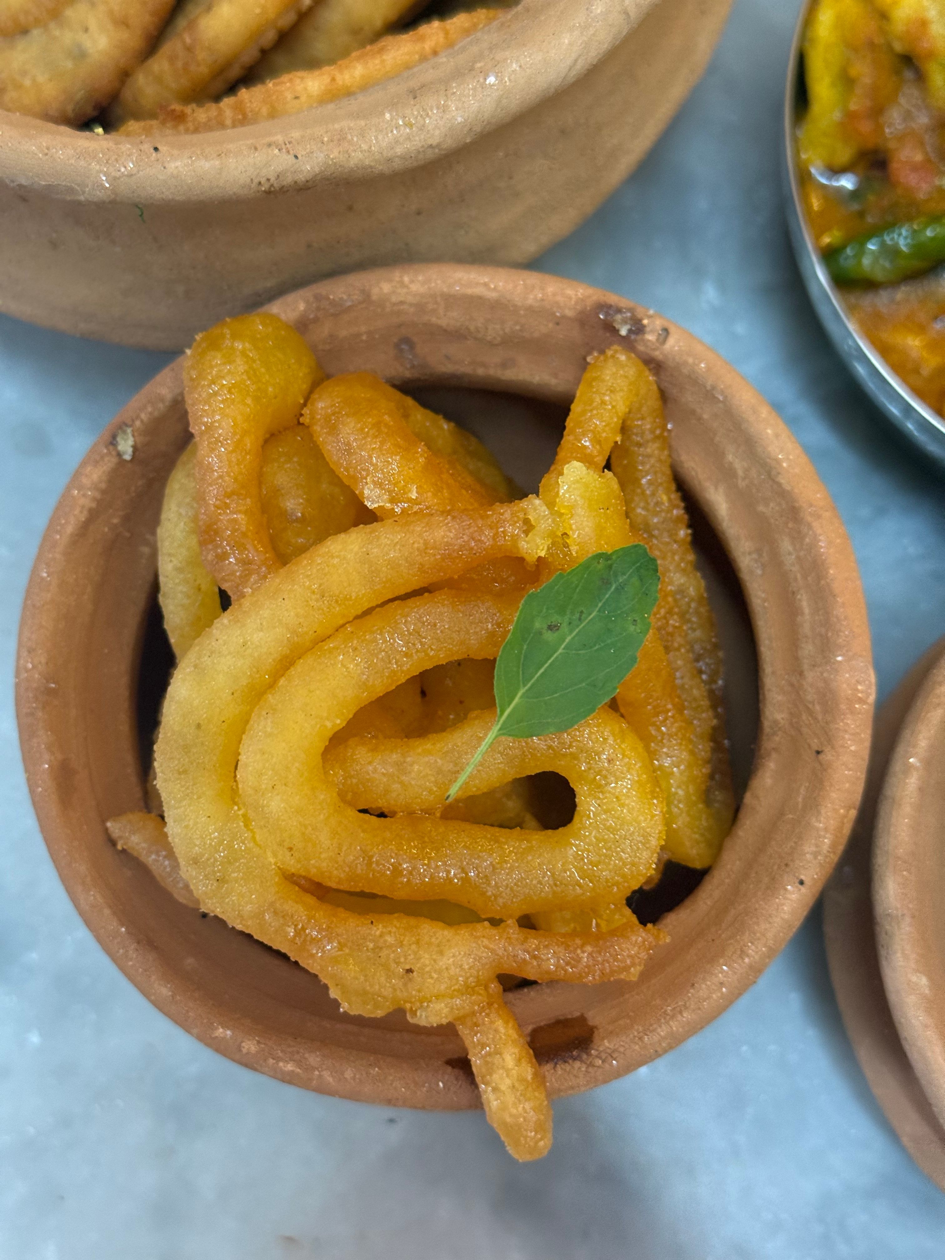 Close-up of traditional Indian Jalebi served in a clay pot garnished with a green leaf.