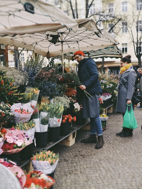 Мужчина в черной куртке и синих джинсовых джинсах покупает цветы