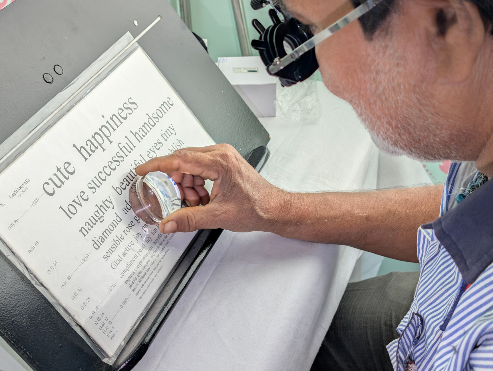 Close-up of a man with glasses reading an eye test chart using a magnifying glass.