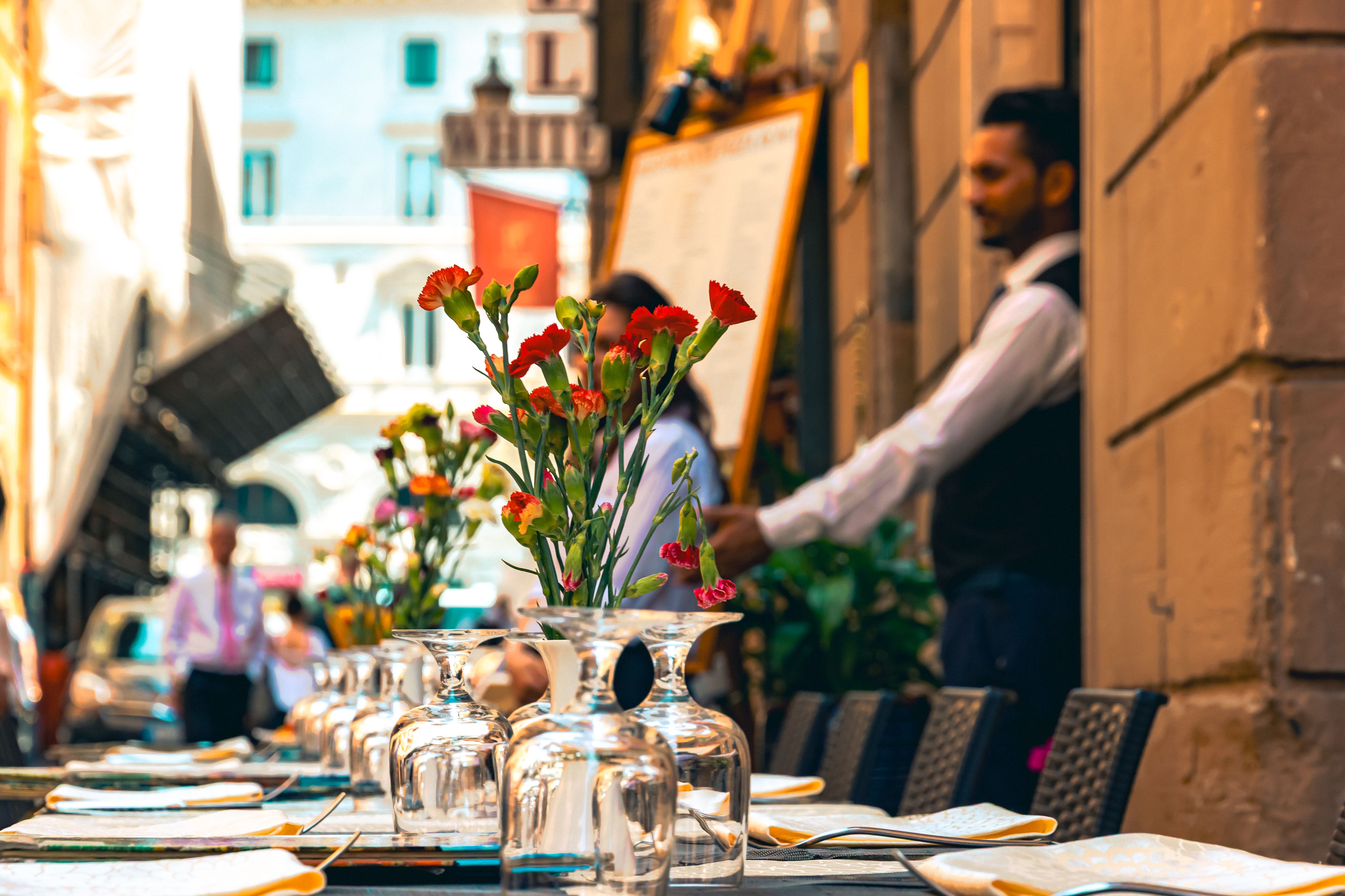 An elegant outdoor restaurant setup in Italy with floral centerpiece, glassware, and attentive service.