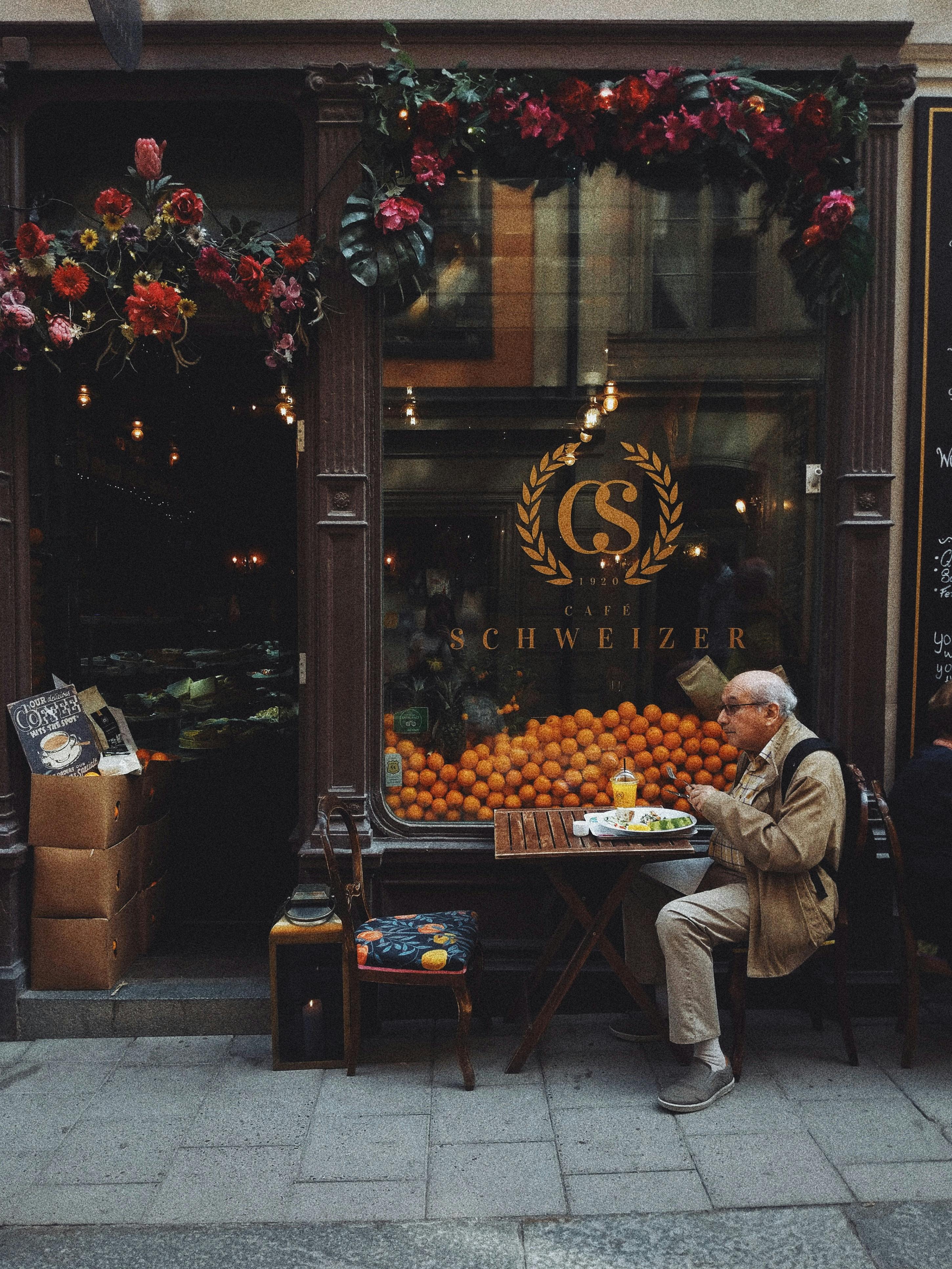 man in brown jacket sitting on chair in front of fruit stand