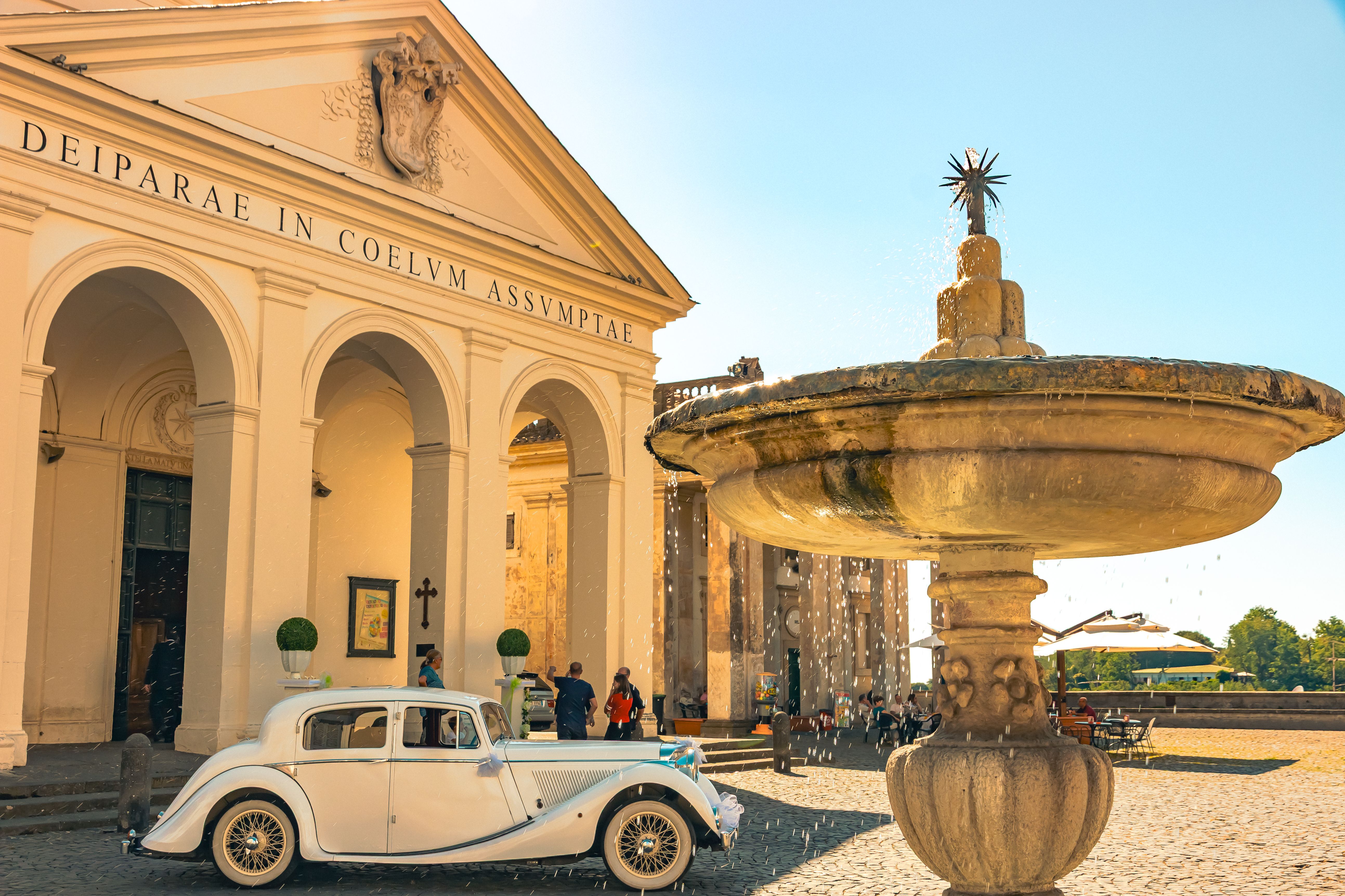 A classic car parked in front of a historic neoclassical building with a fountain.