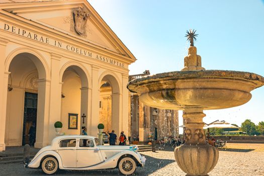 A classic car parked in front of a historic neoclassical building with a fountain.