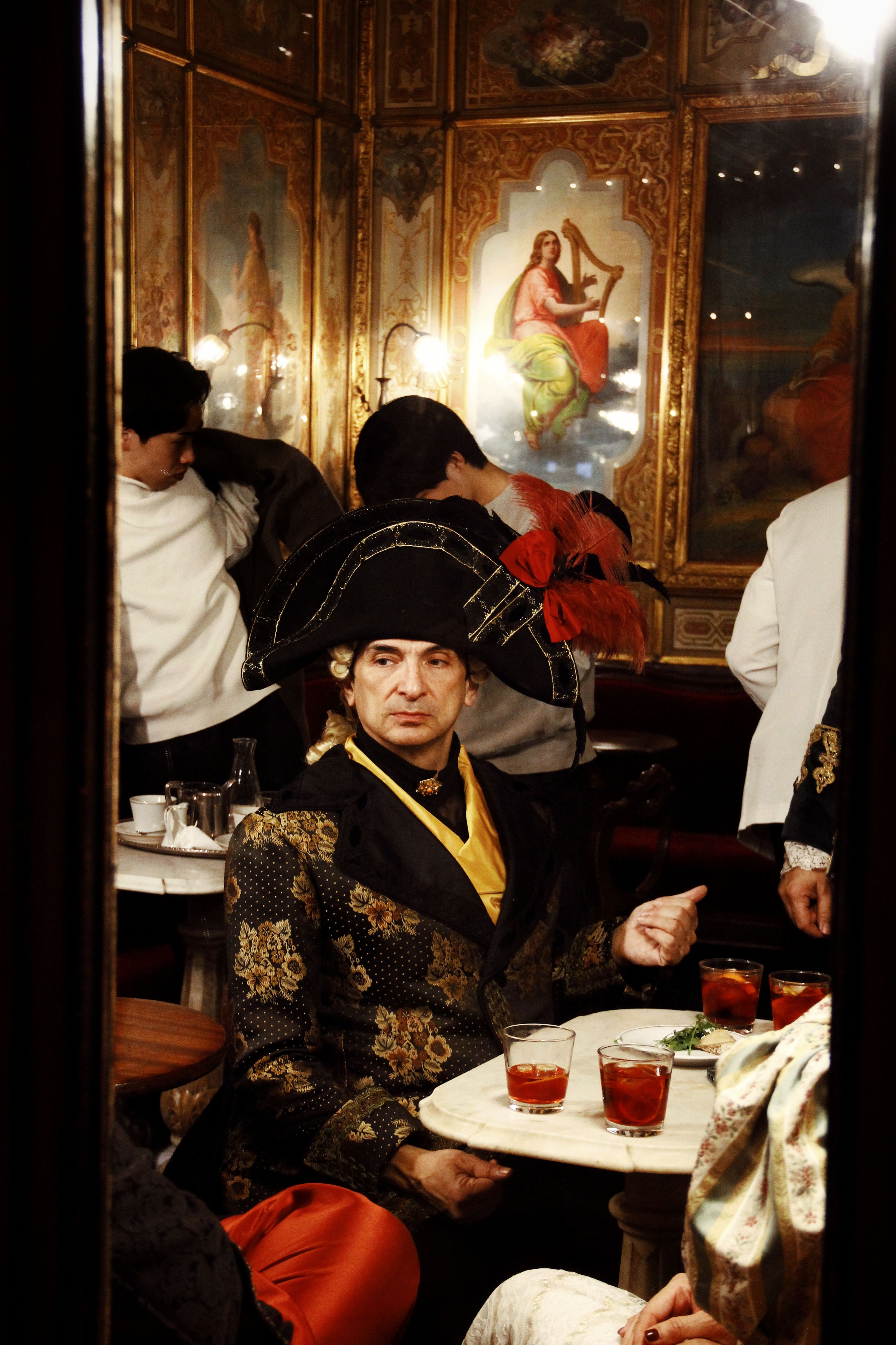 Participants in elaborate costumes enjoy the Venice Carnival in a historic café setting.