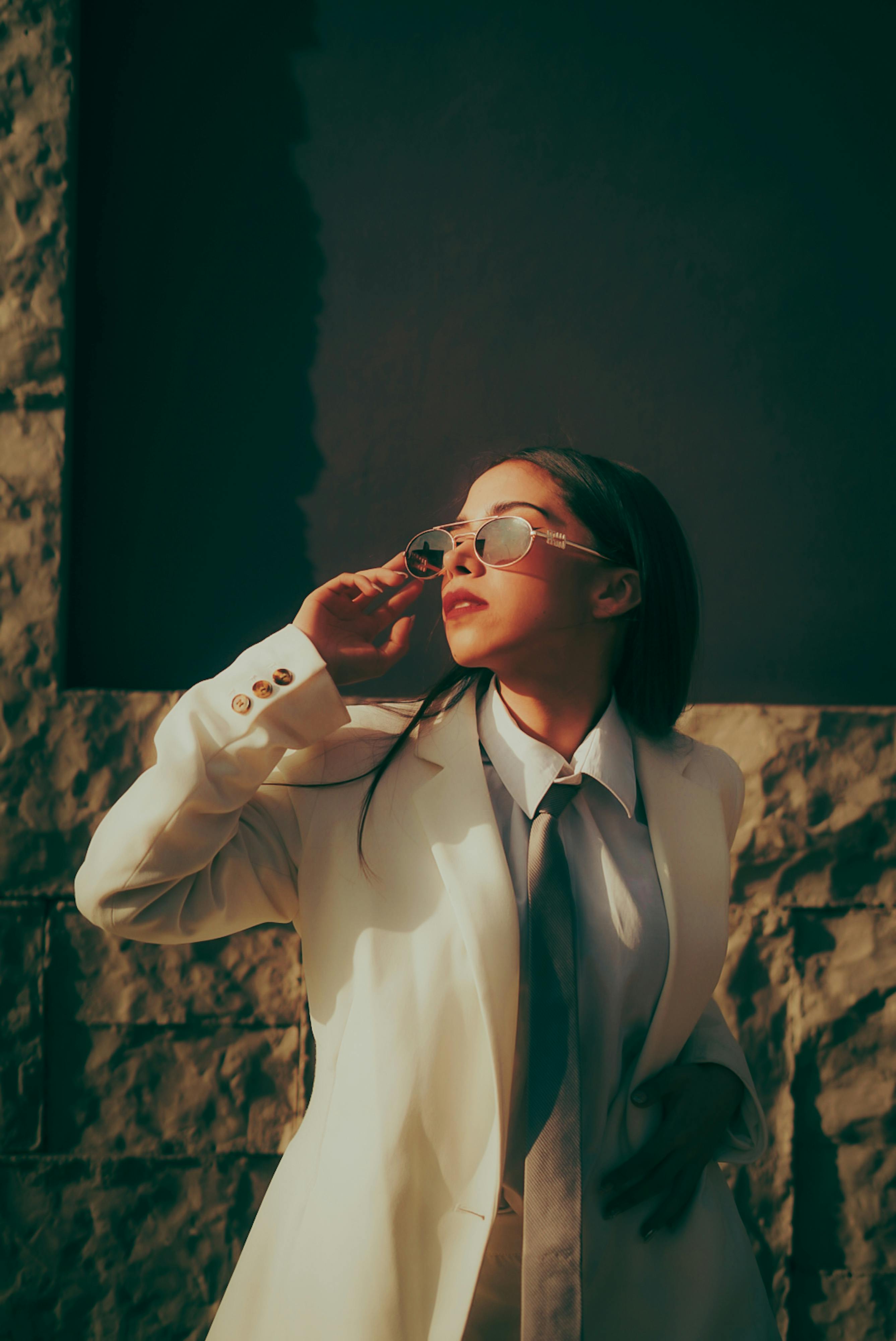 Kostenlos Stilvolle Frau in einem weißen Blazer posiert selbstbewusst im Sonnenlicht und präsentiert moderne Mode. Stock-Foto