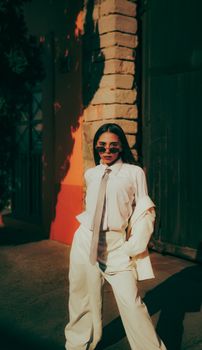 Trendy woman poses confidently in a chic white outfit outside in urban setting.