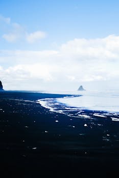 Serene black sand beach with ice pieces under a clear blue sky, perfect for winter travel themes.