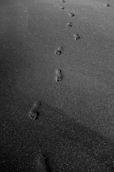 黑色沙滩上，单色的脚印构成了一幅极简而宁静的景色