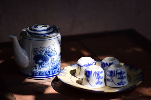 Elegant vintage blue and white teapot with matching cups on a wooden table, creating a cozy classic setting.