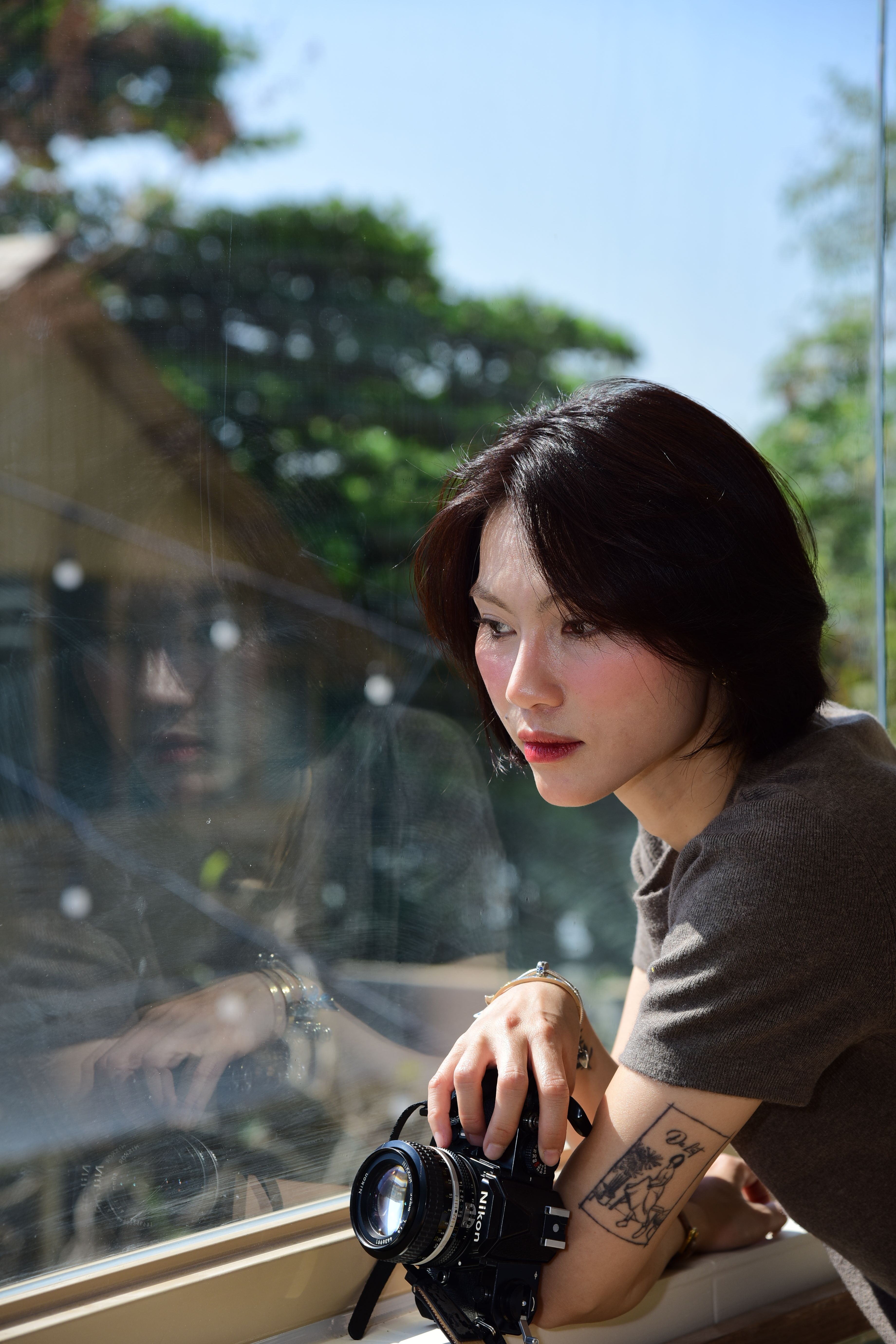 A young woman with a camera pausing thoughtfully by a sunlit window — a quiet moment of self-reflection