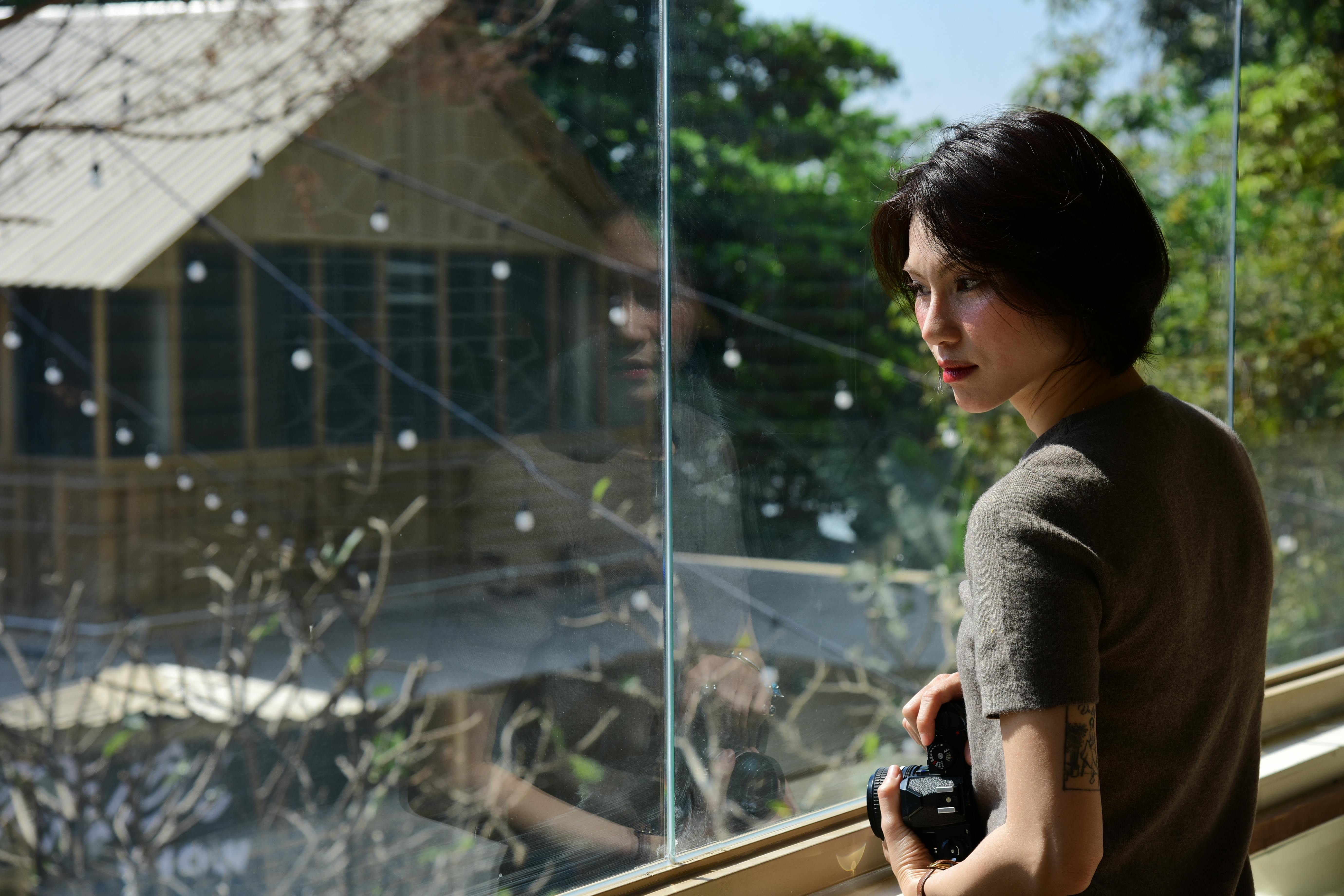 無料 女性がカメラを持って窓の外を見つめており、ガラスに柔らかく映った光景が映っている。 写真素材