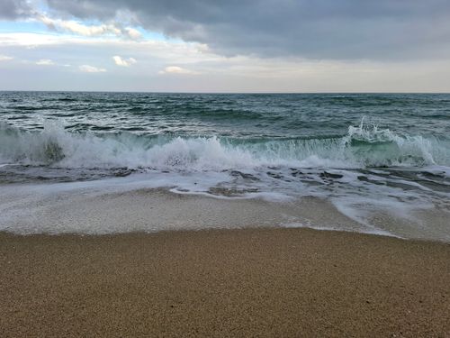 Free Peaceful ocean waves roll onto a sandy beach under a cloudy sky, capturing tranquility and natural beauty. Stock Photo