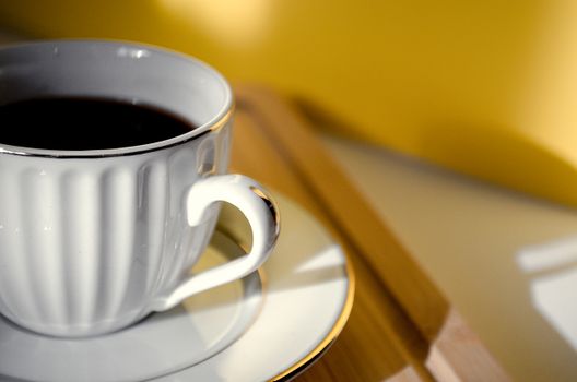 A stylish white coffee cup with black coffee on a bright yellow background, emphasizing modern home aesthetics.