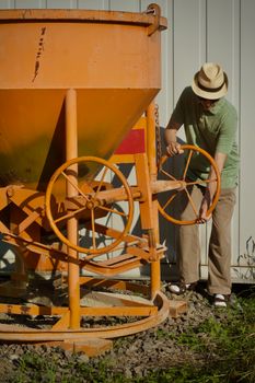 A man interacts with large orange industrial equipment outside a building.