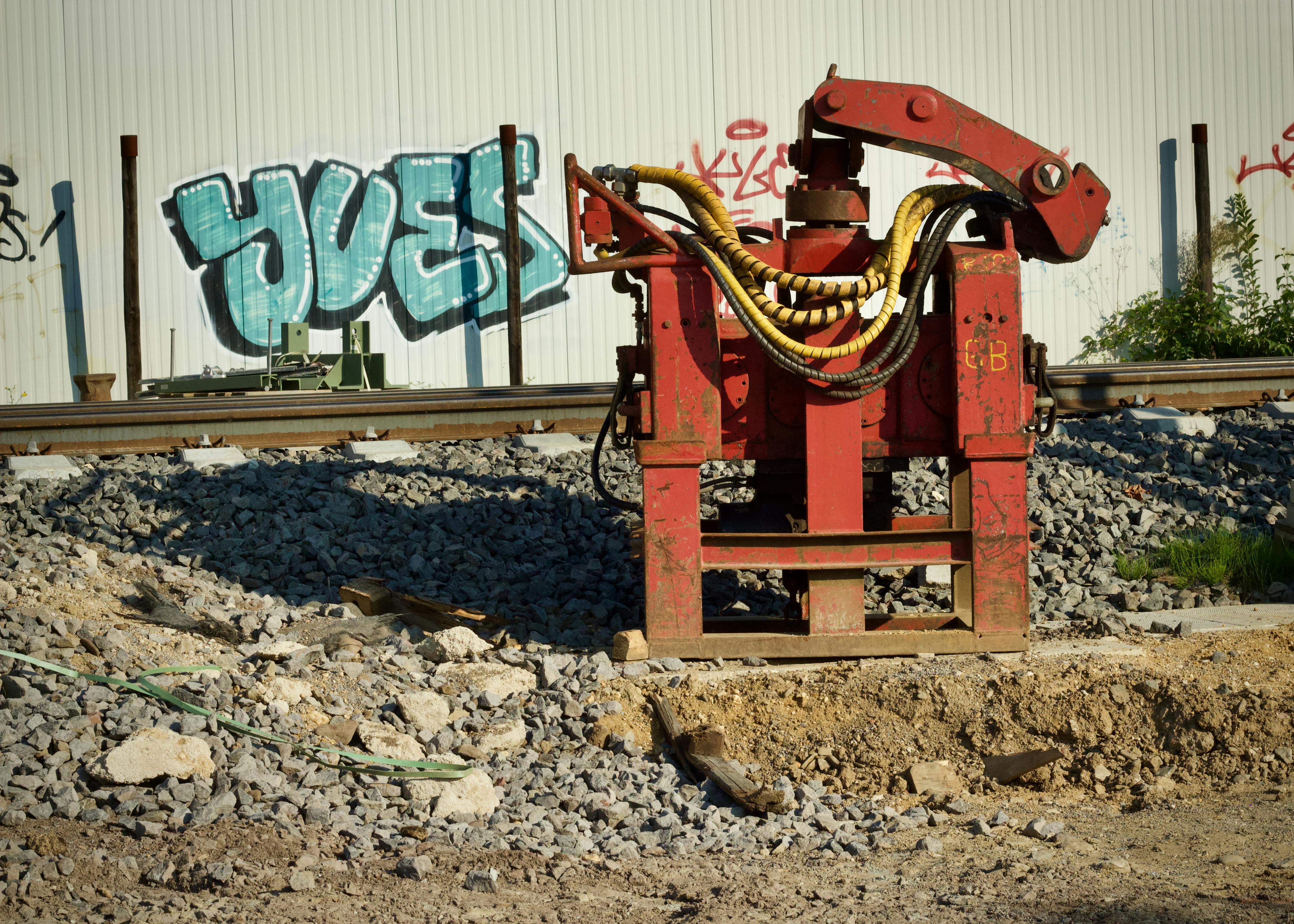 Gratuit Engin de chantier rouge à côté de la voie ferrée et d'un mur de graffitis. Photos