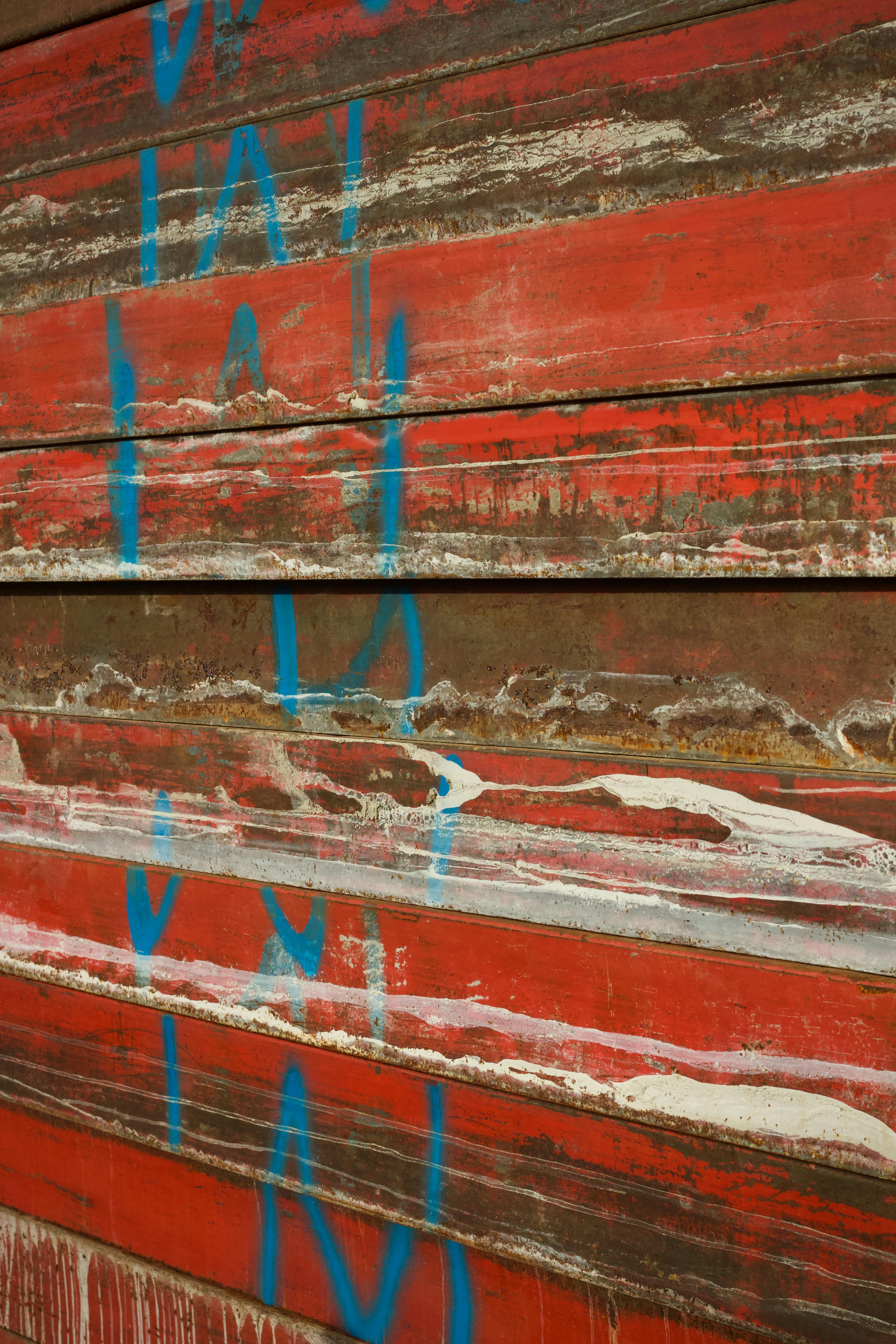 Free Close-up of a rusty red metal wall featuring abstract blue graffiti art design. Stock Photo