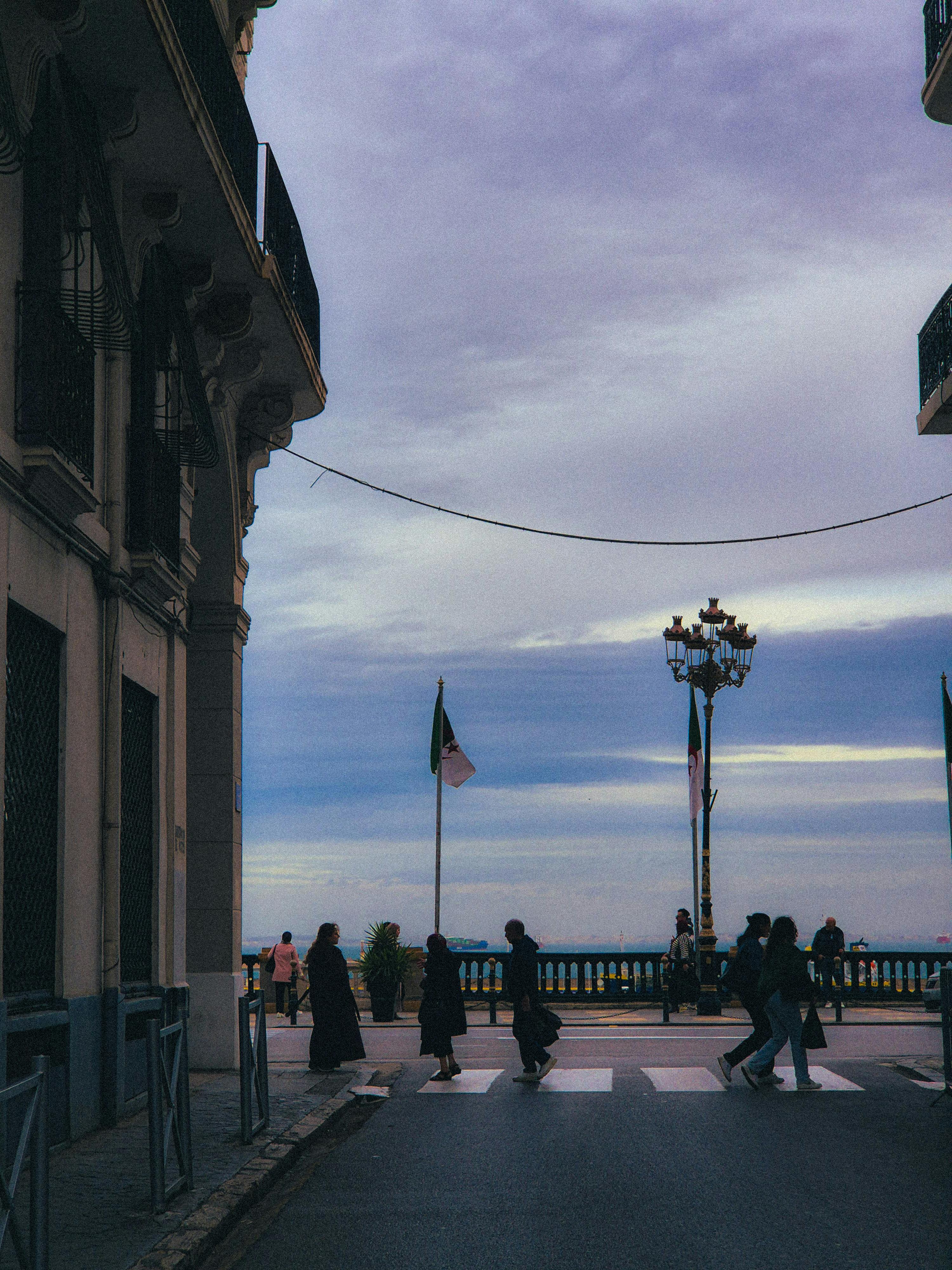 Gratuit Des personnes traversent une rue à Alger, brandissant des drapeaux algériens, avec un magnifique coucher de soleil. Photos