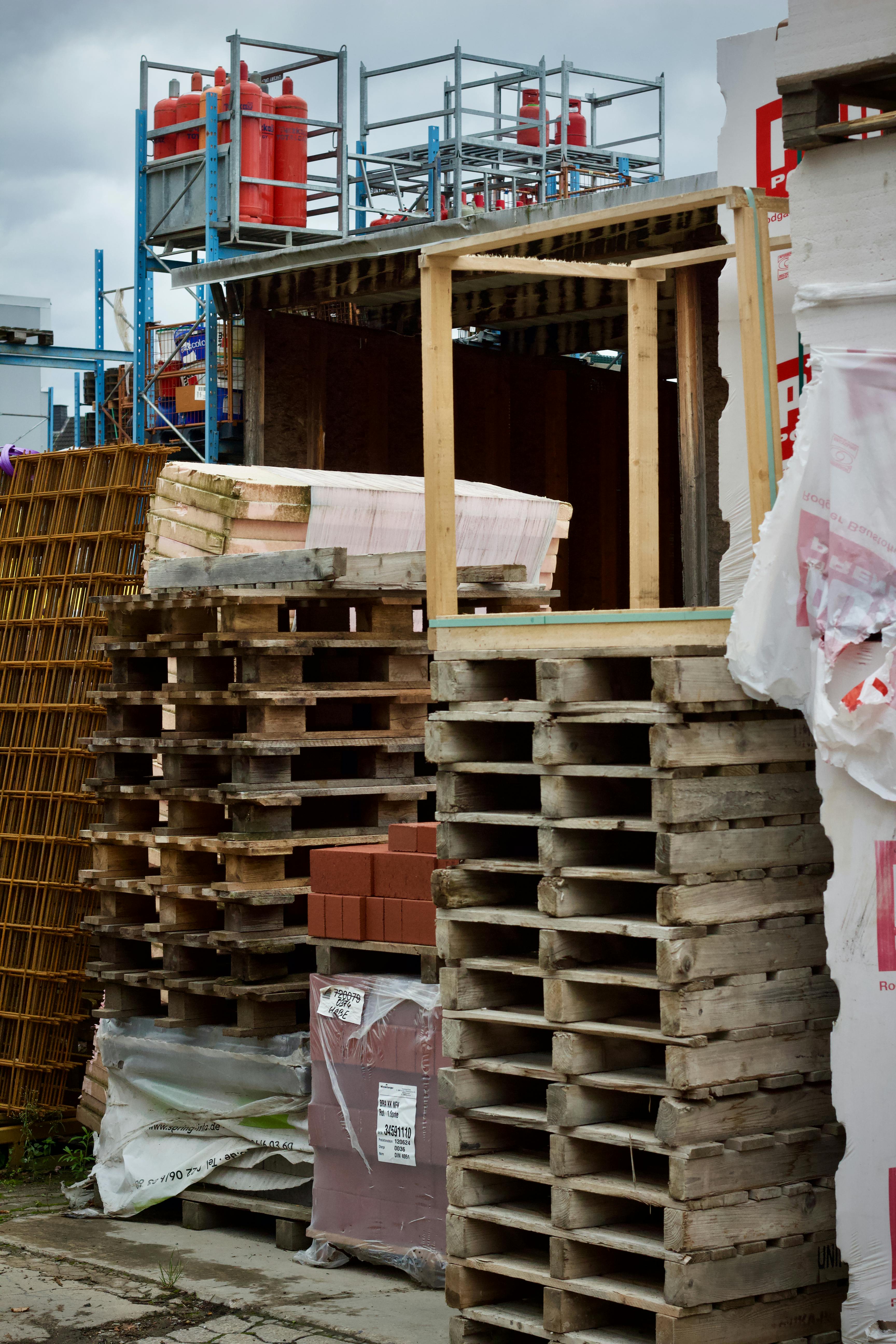 Wooden pallets stacked at an outdoor construction site amidst various building materials.