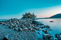 在日落时捕获一个宁静的鹅卵石海滩和一个岩石岛，展示平静的蓝色海水