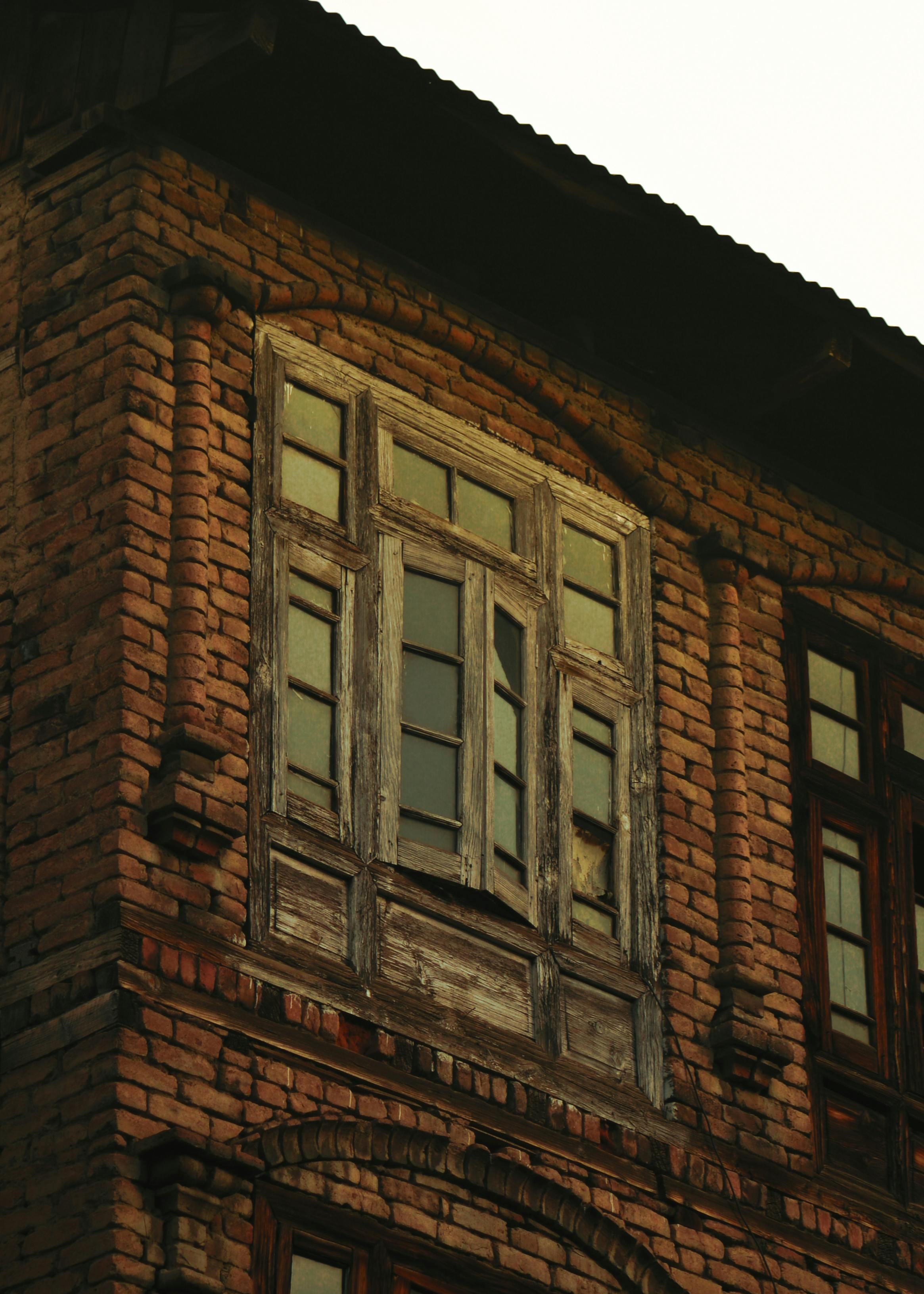Gratis Primo piano della facciata di un edificio d'epoca in mattoni con finestre in legno rustico. Foto a disposizione