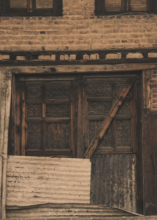 Free A vintage wooden door with intricate patterns set against a rustic brick wall, embodying historic architecture. Stock Photo