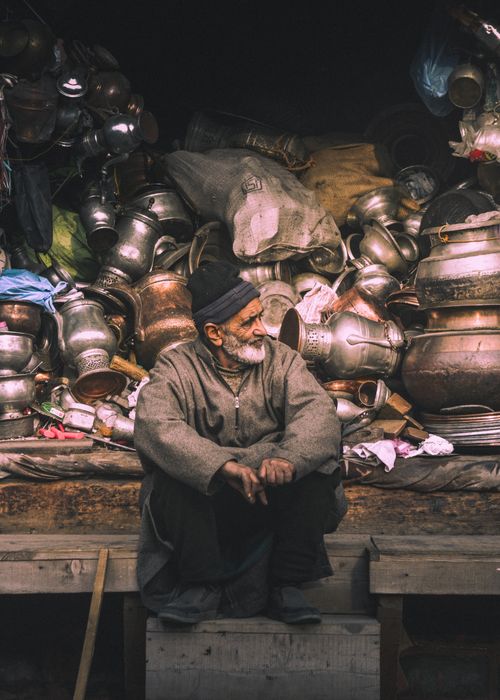 Free An elderly man sitting relaxed in front of an assortment of vintage metal pots. Stock Photo