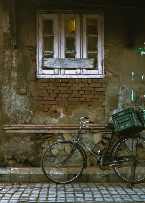 Free Rustic bicycle leaned against an aged, textured wall with a vintage window. Stock Photo