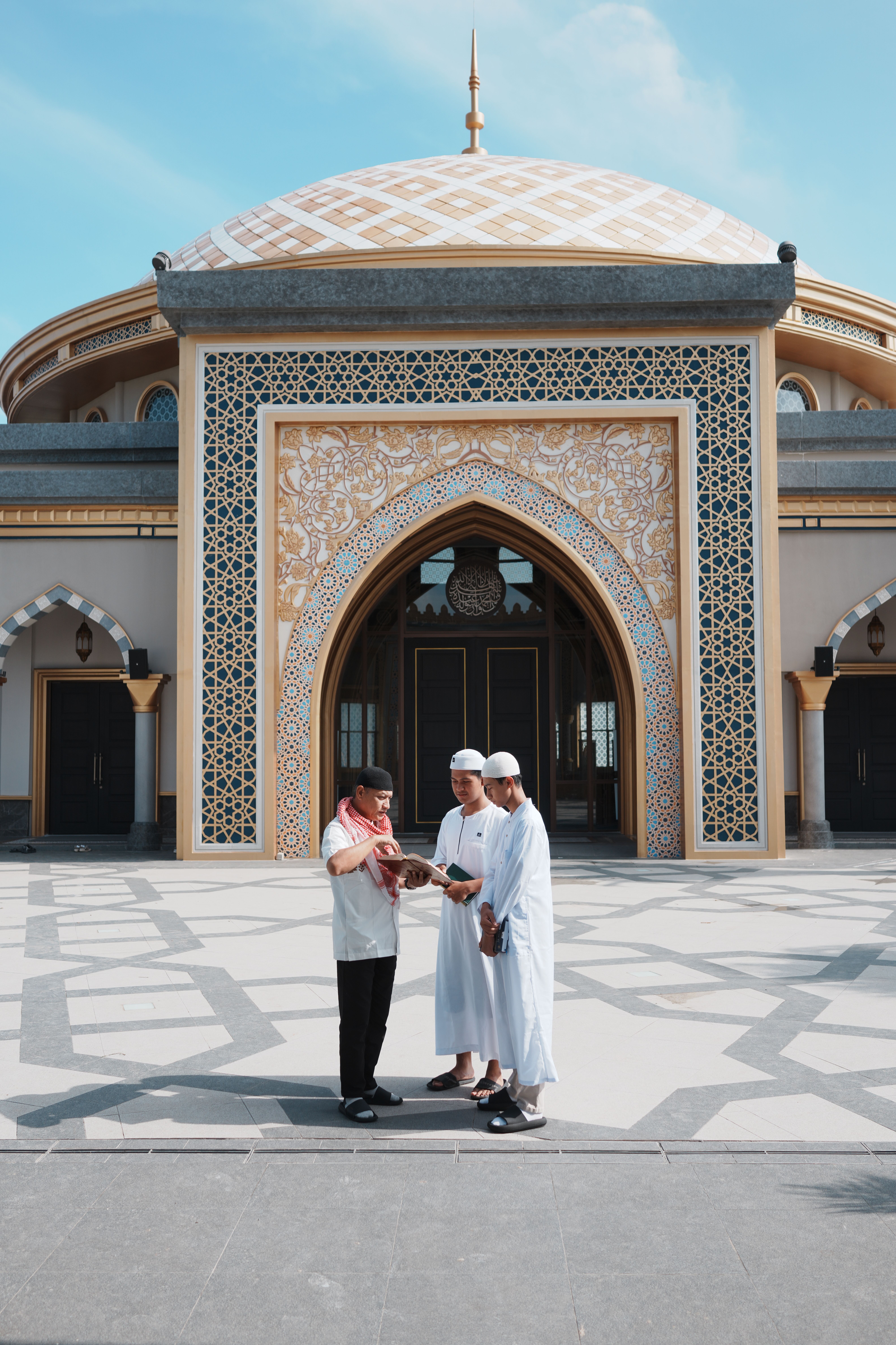 Three men in traditional clothing outside a beautifully designed mosque in Indonesia.