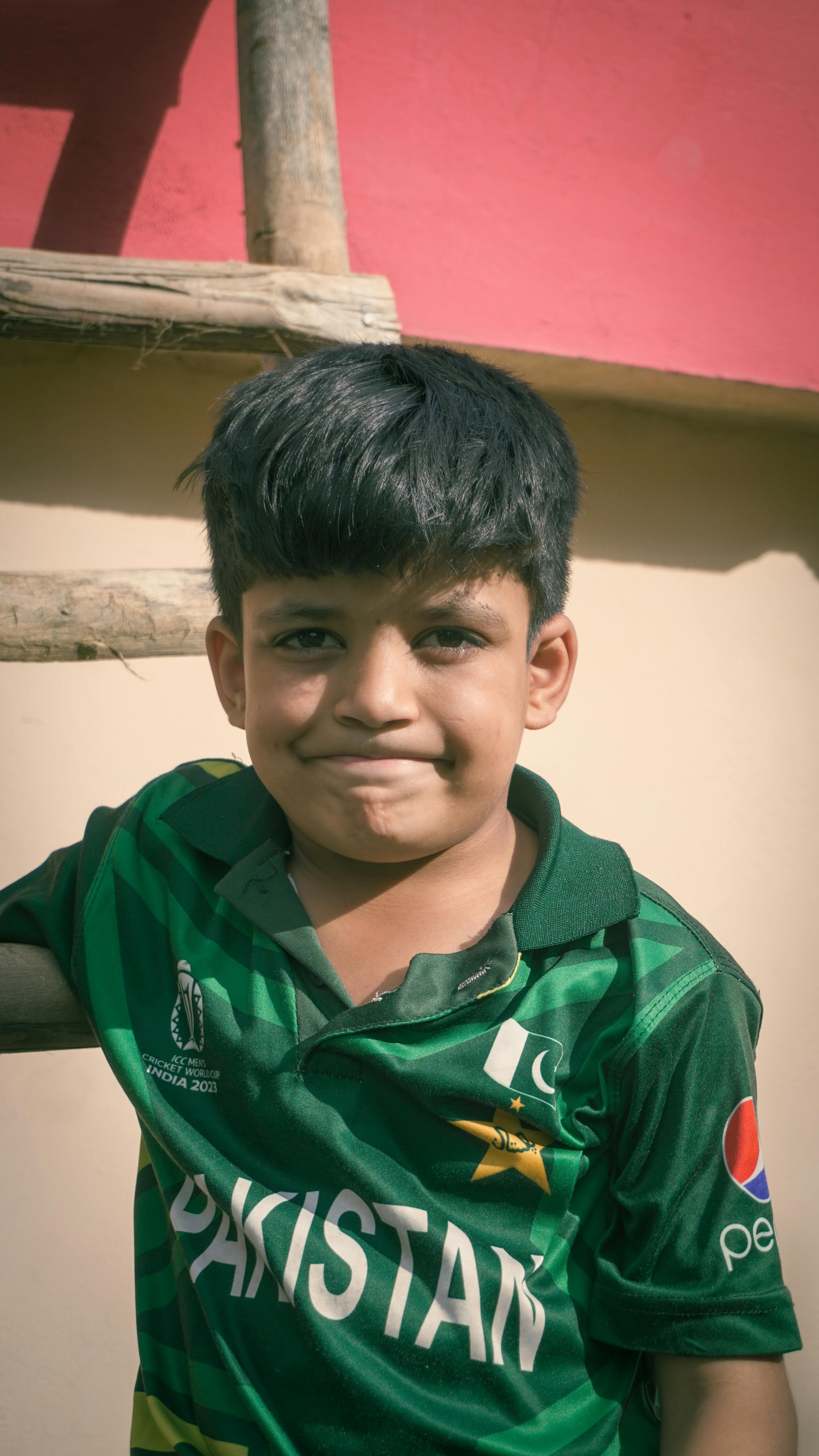 A young boy in a Pakistan cricket jersey poses outdoors in a sunny setting, capturing national pride and enthusiasm.