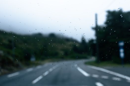 Blurred view of a rainy road in Provence, France, with mountains in the background.