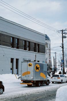 Snowy street scene in Sapporo, Hokkaido featuring delivery truck and cars.