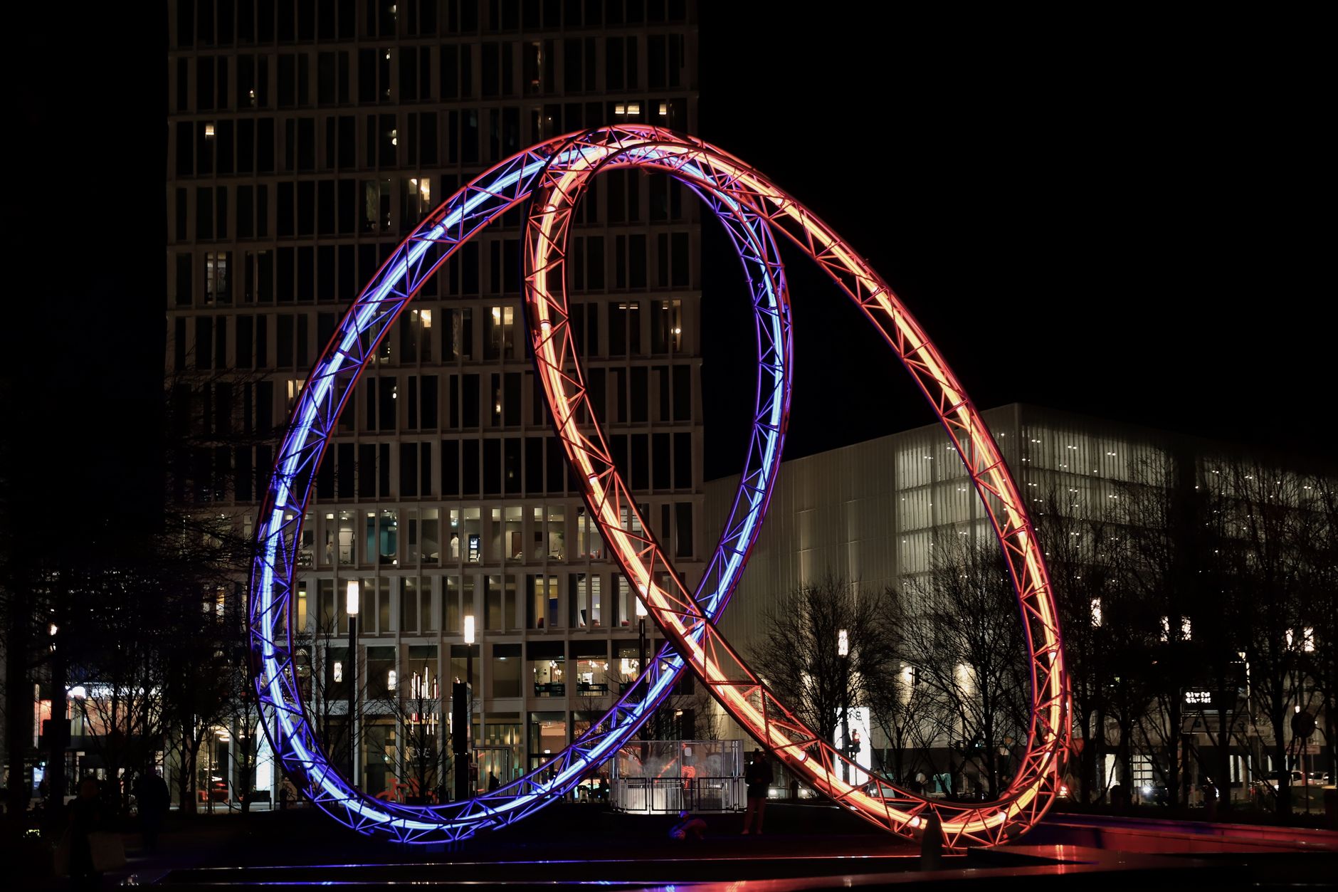 Brightly lit steel sculpture against skyscrapers in Frankfurt at night.