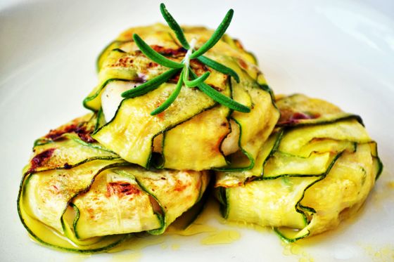 Golden zucchini ribbon parcels filled with melted cheese and topped with rosemary on a white plate