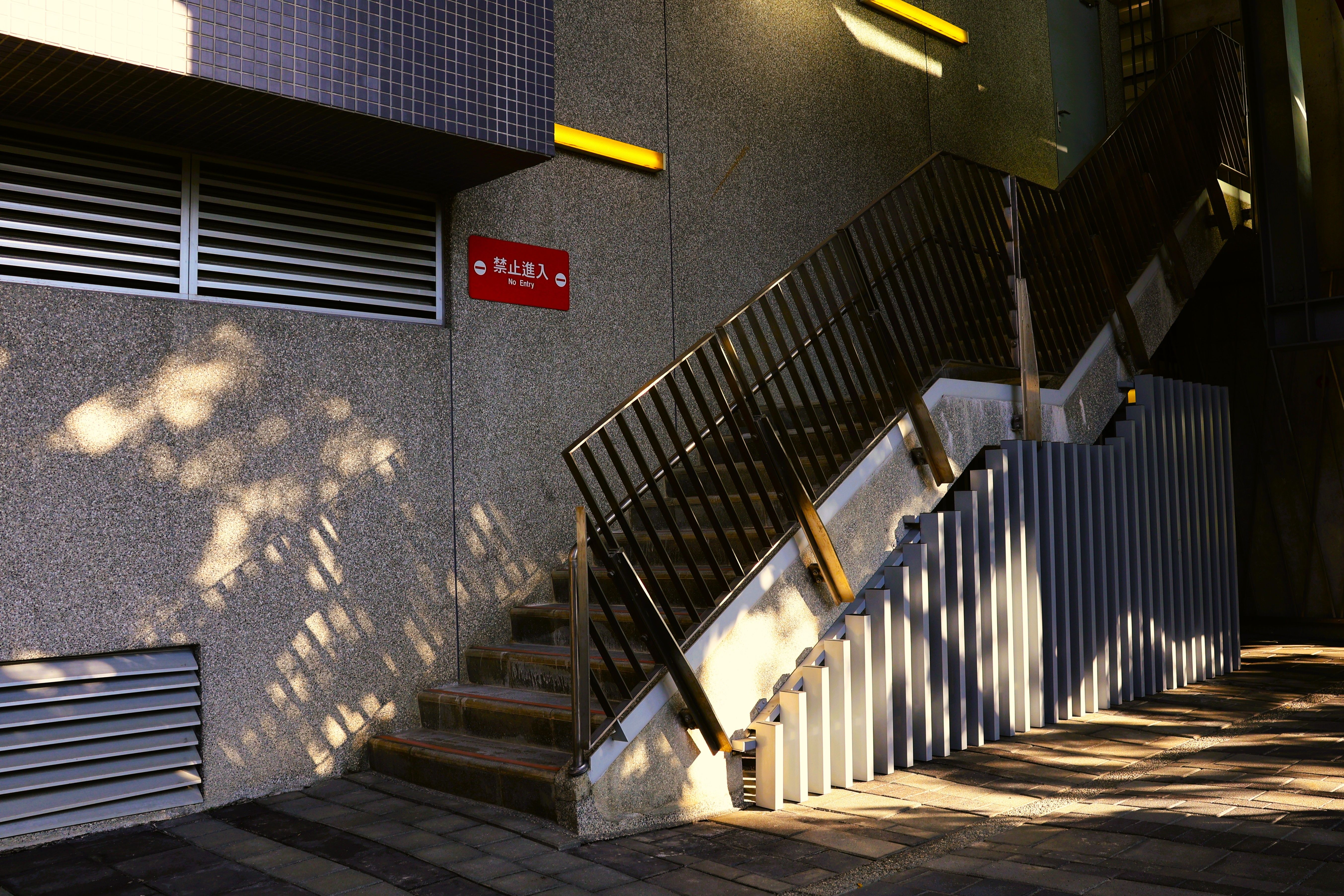 Urban stairs with shadows and a prohibition sign in daylight.