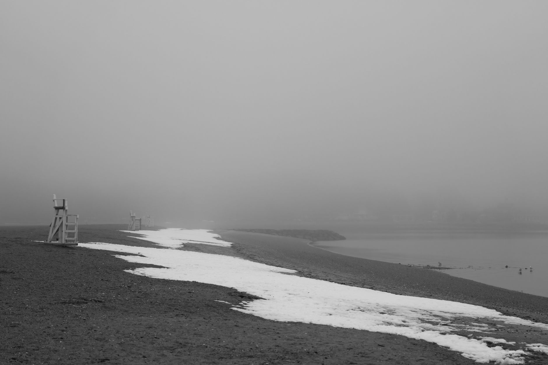 A foggy morning beach scene with lifeguard chairs and snow in Stamford, Connecticut.