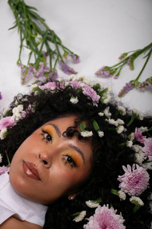 Free Portrait of a woman with curly hair adorned with pink and white florals, evoking a natural aesthetic. Stock Photo