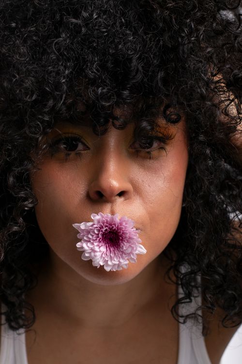 Free Close-up portrait of a woman holding a chrysanthemum flower in her mouth, highlighting natural beauty. Stock Photo