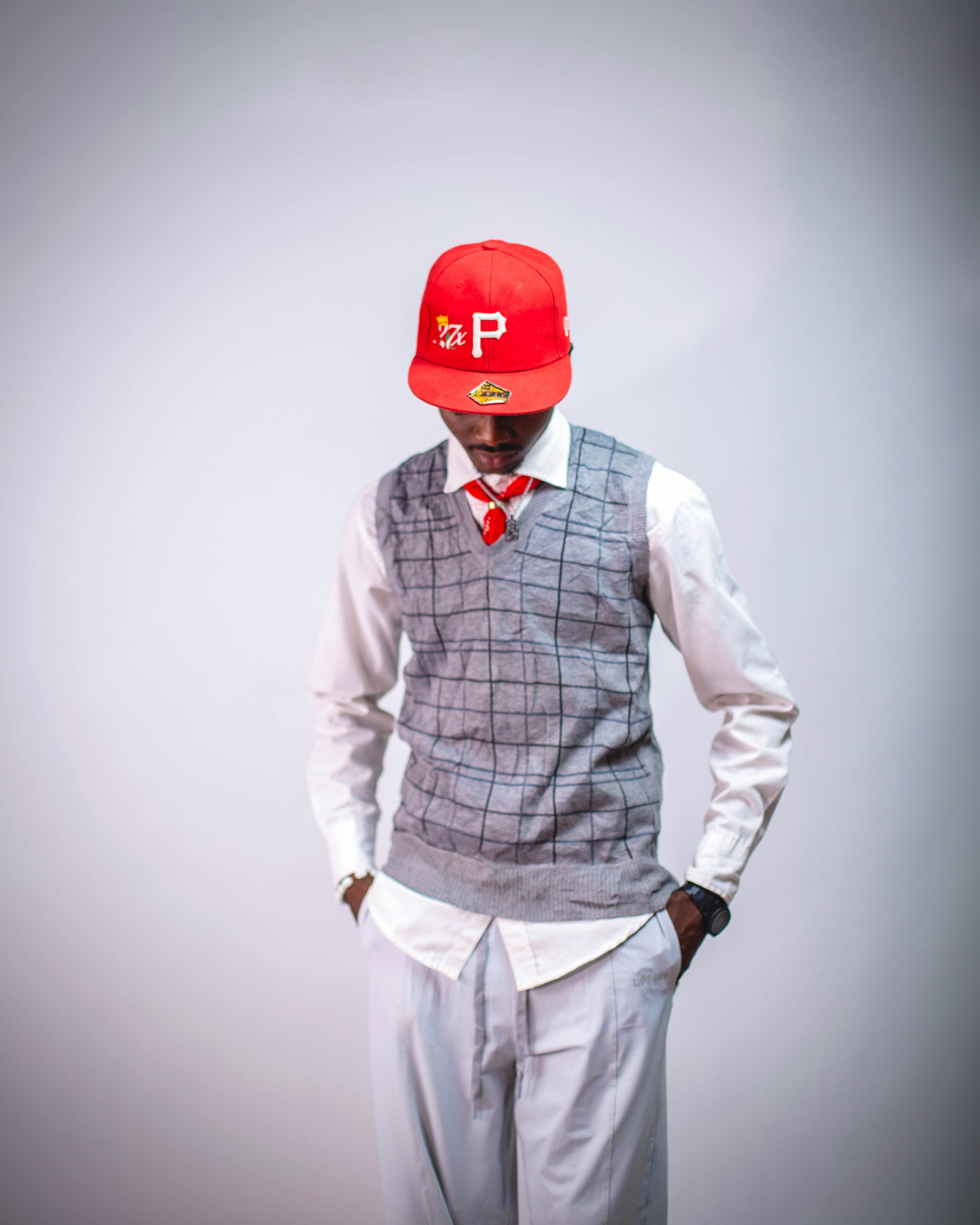 Fashionable man wearing a red cap, grey vest, and white shirt in a studio setting.