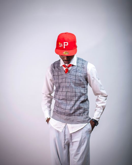 Fashionable man wearing a red cap, grey vest, and white shirt in a studio setting.